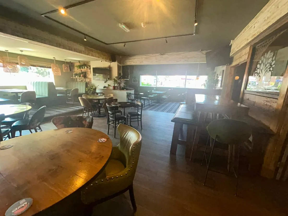 A seating area inside the pub with round tables and green armchairs